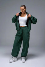 Front View of Green TLF Baggy Track Pants (Women’s GTS Gym-To-Street Edition) featuring side pockets and reflective piping details.
