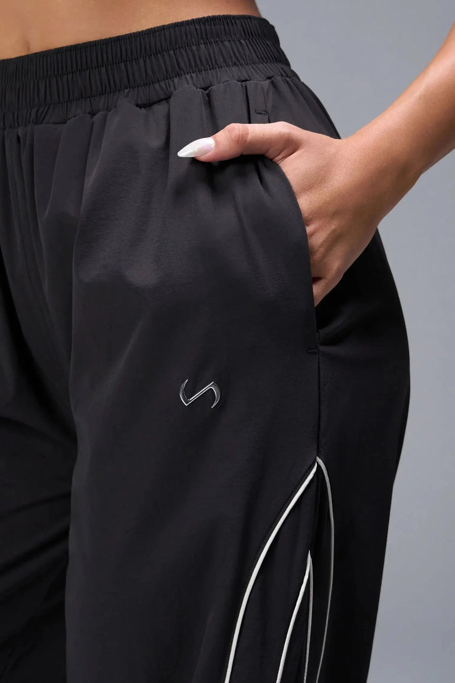 Front View of Black TLF Baggy Track Pants (Women’s GTS Gym-To-Street Edition) featuring side pockets and reflective piping details.