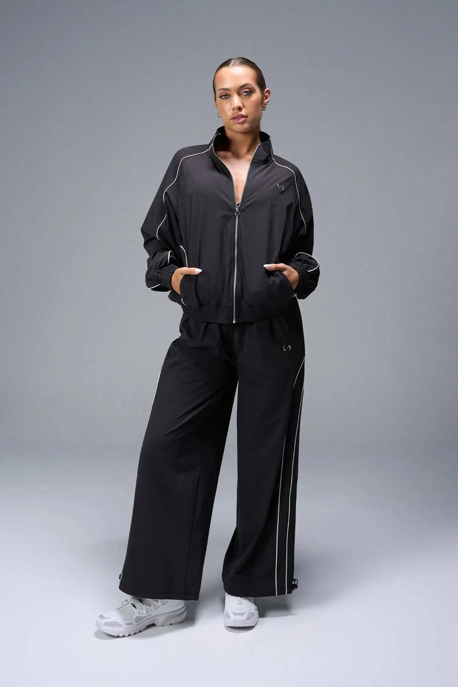 Front View of Black TLF Baggy Track Pants (Women’s GTS Gym-To-Street Edition) featuring side pockets and reflective piping details.