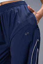 Front View of Blue TLF Baggy Track Pants (Women’s GTS Gym-To-Street Edition) featuring side pockets and reflective piping details.