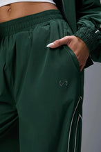 Front View of Green TLF Baggy Track Pants (Women’s GTS Gym-To-Street Edition) featuring side pockets and reflective piping details.